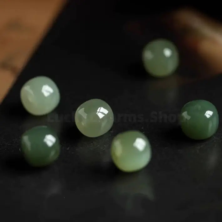 Loose natural Hetian jade beads scatter-placed on dark stone board for jewelry craft display.