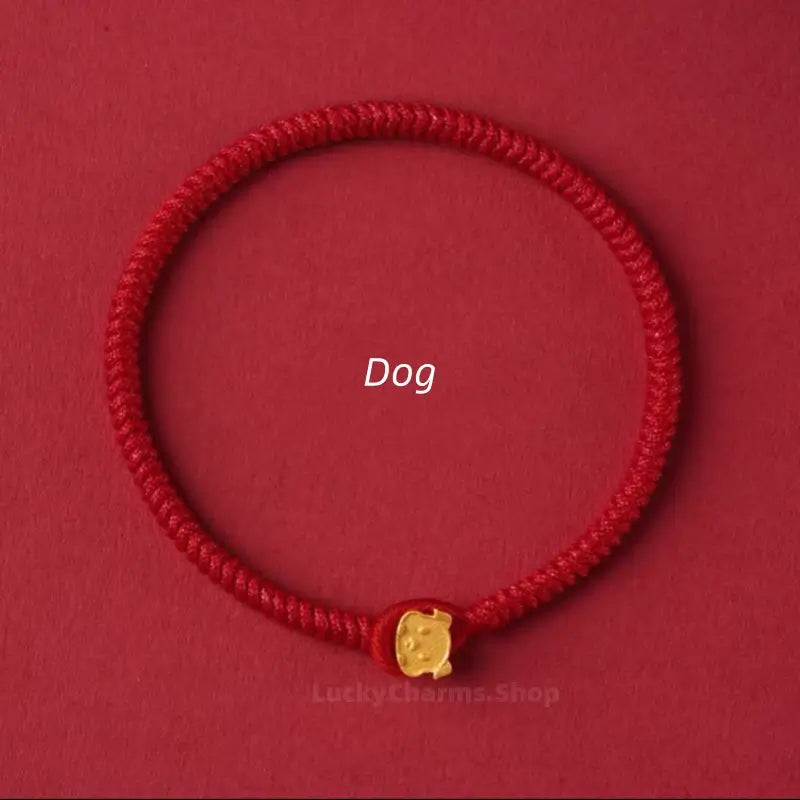 Handwoven red string protection bracelet featuring a small gold Dog zodiac charm clasp on red surface.