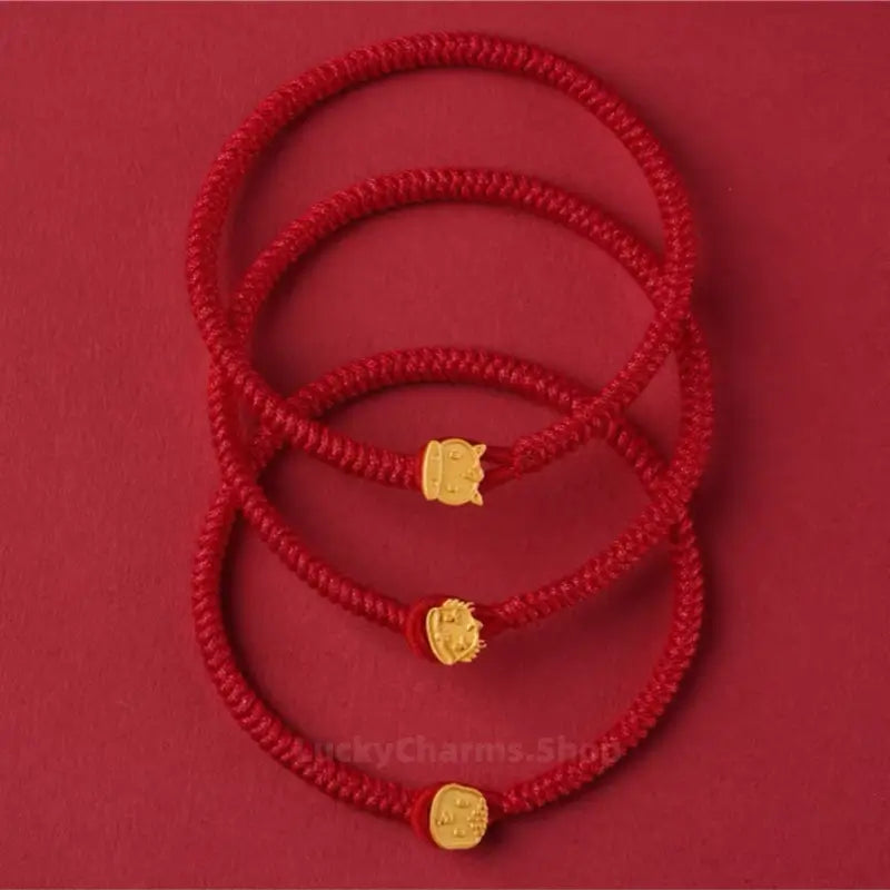 Three handwoven red string lucky bracelets stacked vertically, each featuring a gold Chinese zodiac animal clasp.