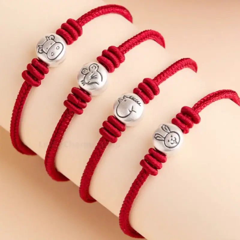 Four braided red string bracelets featuring 999 fine silver Chinese zodiac animal beads lined up together.