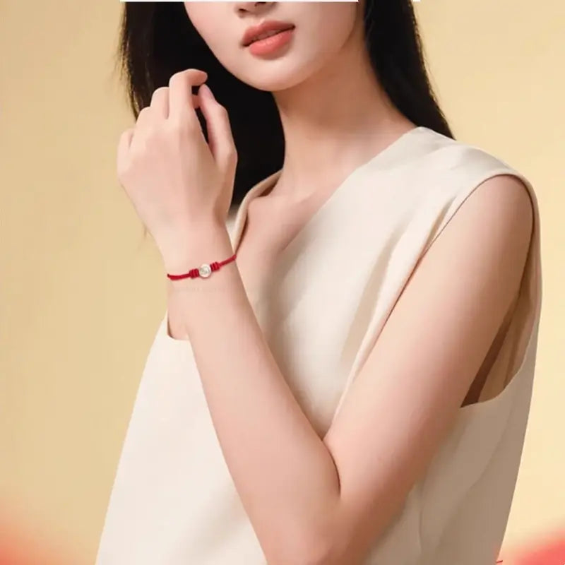 Woman wearing a delicate braided red string bracelet with a 999 fine silver Chinese zodiac charm bead.