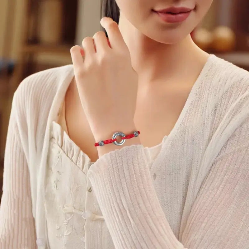 Woman wearing red braided string bracelet with S999 fine silver peace buckle and fortune beads.
