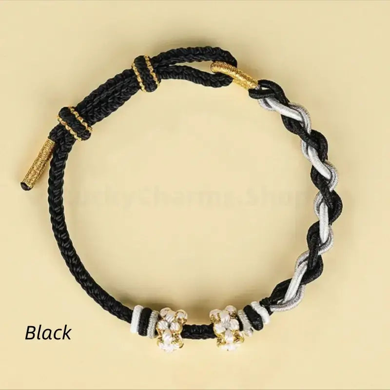 Black and silver-gray twisted braided cord bracelet with white peach blossom knots and gold thread accents.