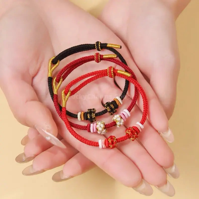 Hand holding red and black braided cord bracelets featuring handcrafted peach blossom knot beads.