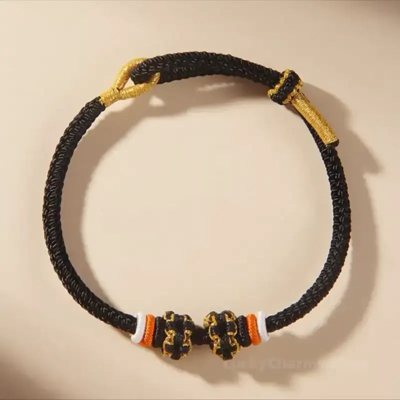 Black braided rope bracelet with gold accent loops and DIY peach blossom knot beads.