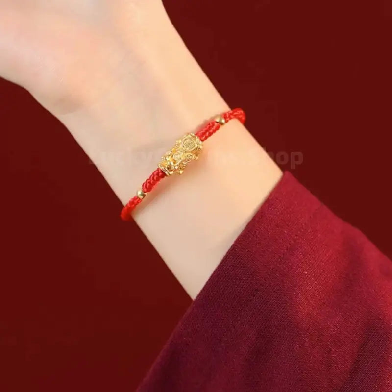 Woman wearing gold-plated silver Pixiu fortune bracelet on red braided string around wrist.