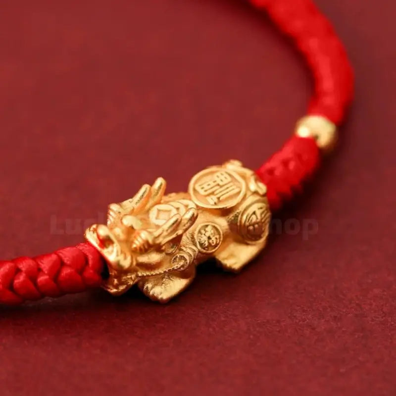 Extreme close-up of 3D gilded silver Pixiu charm with fortune coin engravings on red cord.