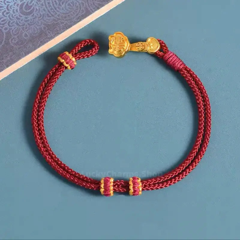 Dark red braided hand rope bracelet with a gold-plated Ruyi clasp and woven spacer rings.