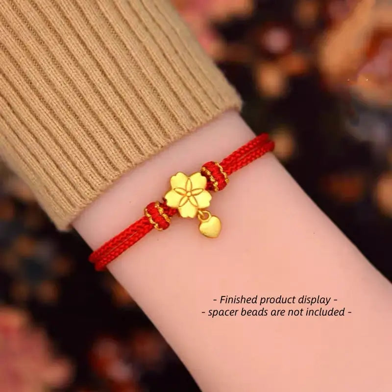 Red braided string bracelet styled on wrist with a gold plum blossom charm pendant.