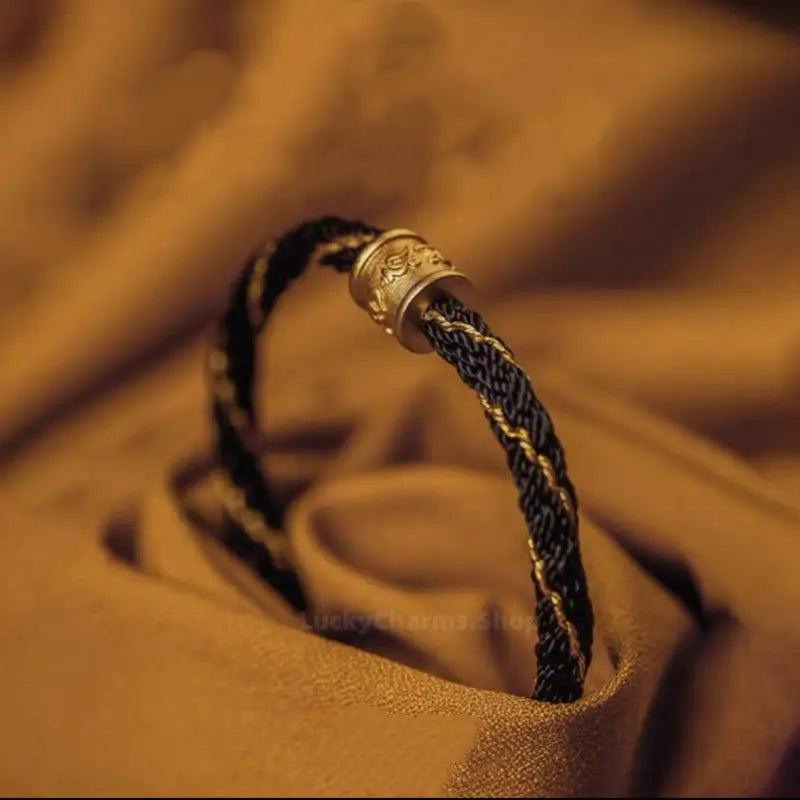 Black and gold braided Tibetan cord bracelet featuring a gold carved Six-Syllable Mantra turning bead charm.