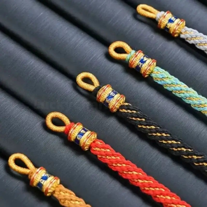 Close-up of colorful braided cord bracelets showing loop clasps and gold Six-Syllable Mantra turning beads.