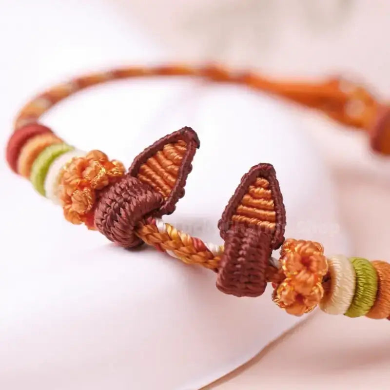Macro view of handmade braided orange rope bracelet showing woven Nick fox ears detail.