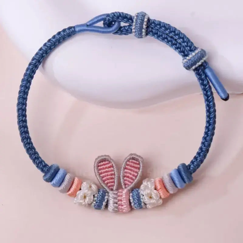 Handmade braided blue rope bracelet featuring pink and grey woven Judy rabbit ears charm.