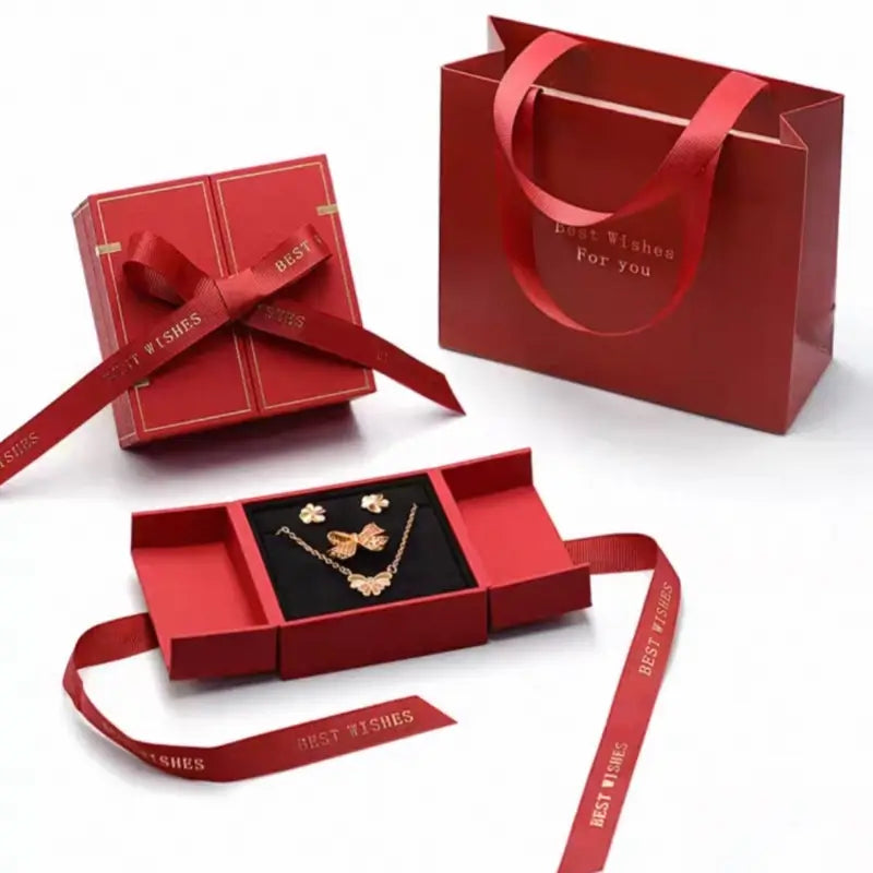 Red ribbon double-opening jewelry box set displayed open with necklace and closed next to matching gift bag.