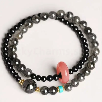 Natural black obsidian and rutilated quartz double-strand protection bracelet with a pink rose quartz don't charm on a white background