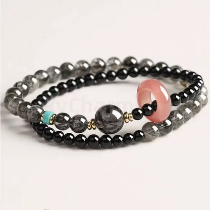 Double-layer black crystal energy bracelet showcasing a large rutilated quartz bead, gold accents, and a bright turquoise spacer