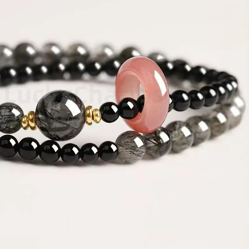 Close-up macro shot of a black blessing bracelet highlighting a glossy pink quartz safety donut charm and shiny obsidian beads