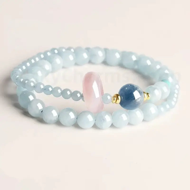 Natural aquamarine light blue double-strand bracelet with a pink rose quartz donut and dark blue kyanite bead on a white background
