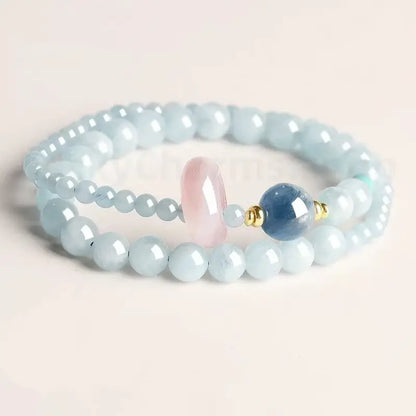 Natural aquamarine light blue double-strand bracelet with a pink rose quartz donut and dark blue kyanite bead on a white background