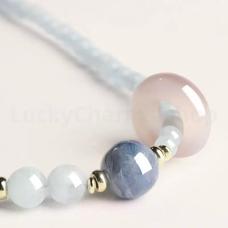 Macro shot of a blue kyanite crystal main bead and a smooth translucent pink quartz charm on a healing gemstone bracelet