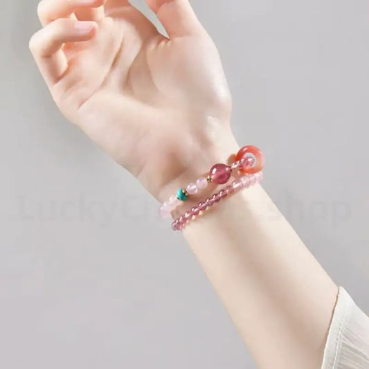 A woman raising her hand while wearing the natural strawberry quartz pink crystal beaded bracelet for an elegant style