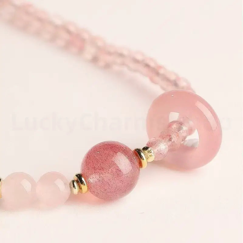 Close-up detail of a large pink strawberry quartz healing crystal main bead with gold accent hardware on a multi-layer bracelet