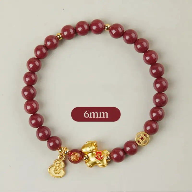 A delicate 6mm natural cinnabar beaded bracelet with gold-plated sterling silver horse, coin, and Wu Lou gourd charms.