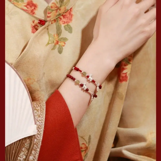 Side profile of a woman in a traditional outfit wearing red cinnabar and Hetian jade beaded bracelets for positive energy.