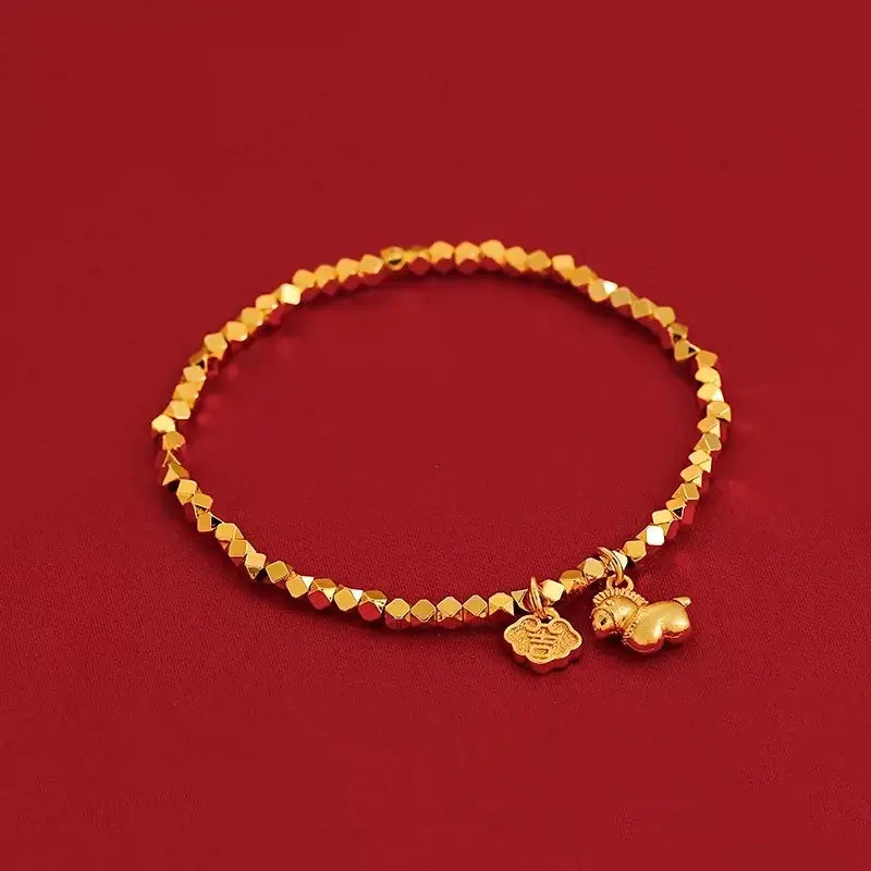 A delicate gold-plated bracelet made of faceted geometric beads, featuring a tiny horse charm and a Ruyi lock amulet on a rich red background.