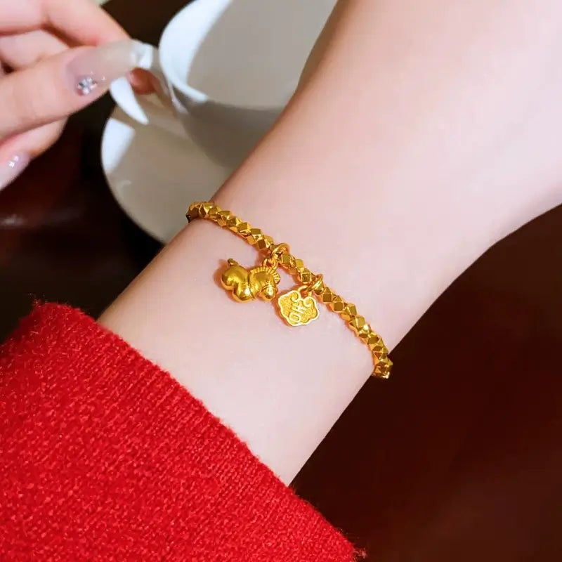 Lifestyle close-up of a woman's wrist wearing the gold-plated textured bead bracelet with dangling lucky charms, next to a white coffee cup.