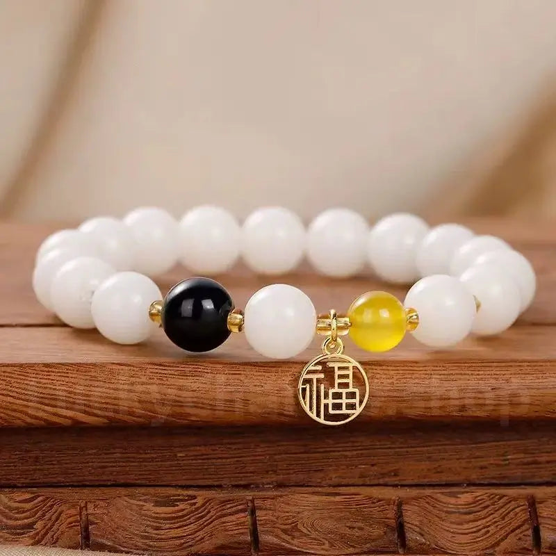 An 8mm white jade bodhi seed bracelet on a wooden stand, featuring a glossy black agate bead, a yellow spacer bead, and a gold Fu fortune charm.
