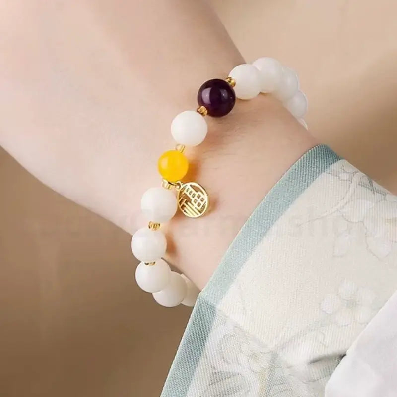 Close-up of the 8mm white jade bodhi seed fortune bracelet on a woman's wrist, highlighting the dangling gold-plated Chinese blessing amulet.
