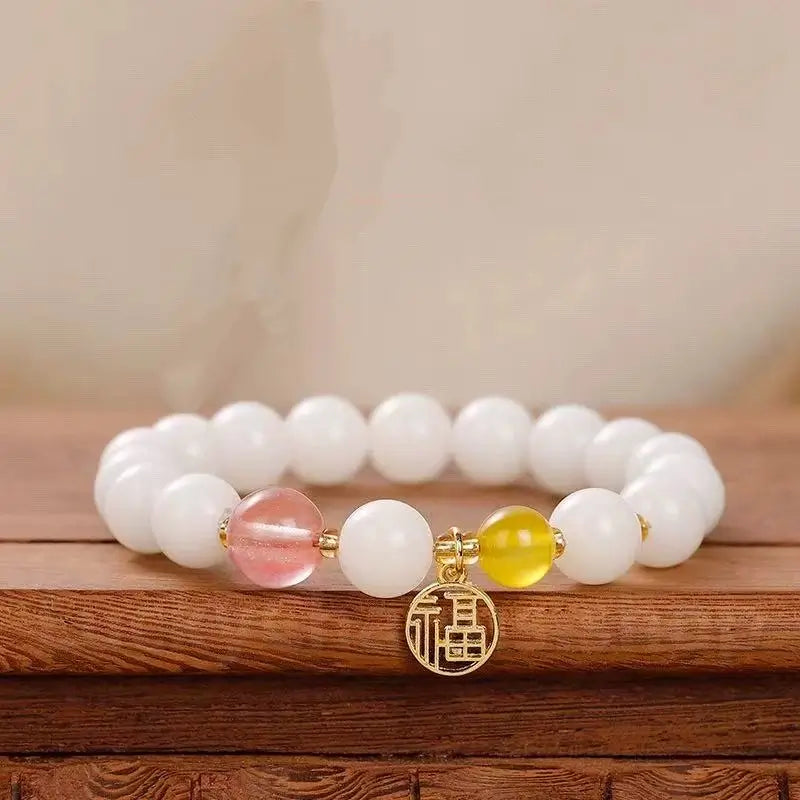 A luck-blessing bracelet made of 8mm white jade bodhi seeds, accented with a translucent pink strawberry quartz bead and a gold fortune amulet.