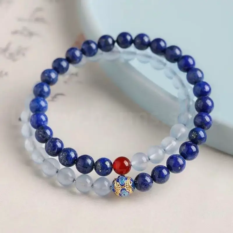 An angled view of the double-layer lapis lazuli and aquamarine protection bracelet, showcasing the 6mm round crystal beads with the gold-plated enamel blessing amulet.