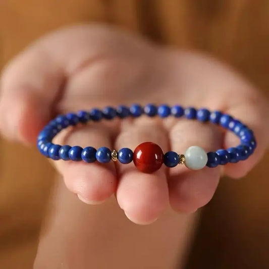 A 4mm natural lapis lazuli single-layer protection bracelet presented on an open palm, highlighting the vibrant contrast of blue, red, and gold.