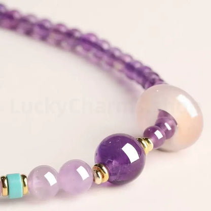 Close-up detail of a natural purple amethyst bracelet showing a glossy crystal bead, gold spacers, and a turquoise accent bead