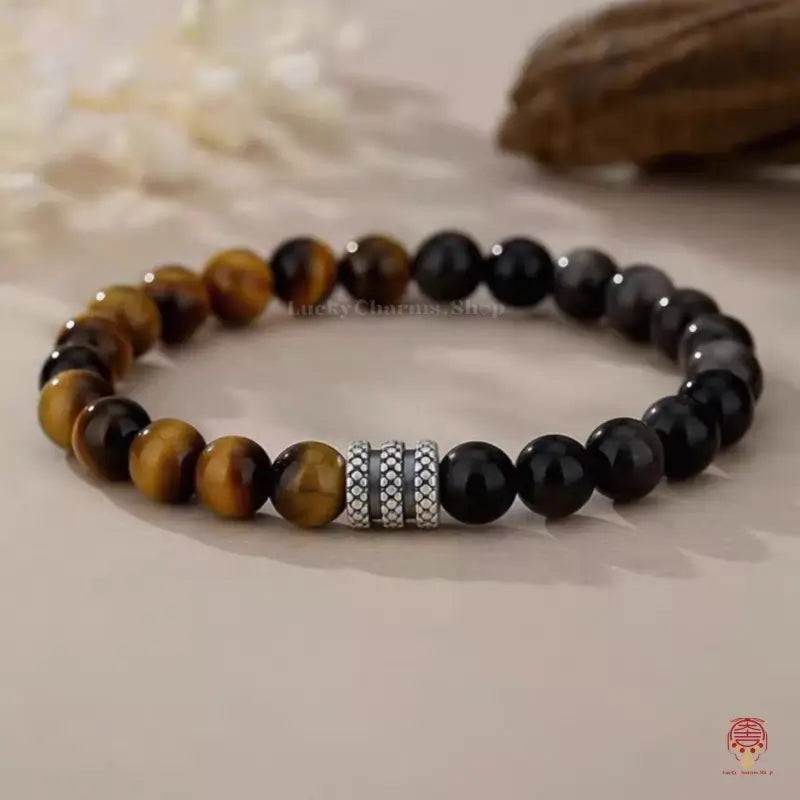 Ground level shot of a yellow tiger's eye and black obsidian luck bracelet focused on patterned silver rings.