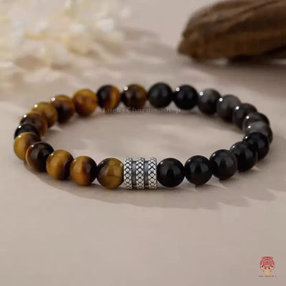 Ground level shot of a yellow tiger's eye and black obsidian luck bracelet focused on patterned silver rings.