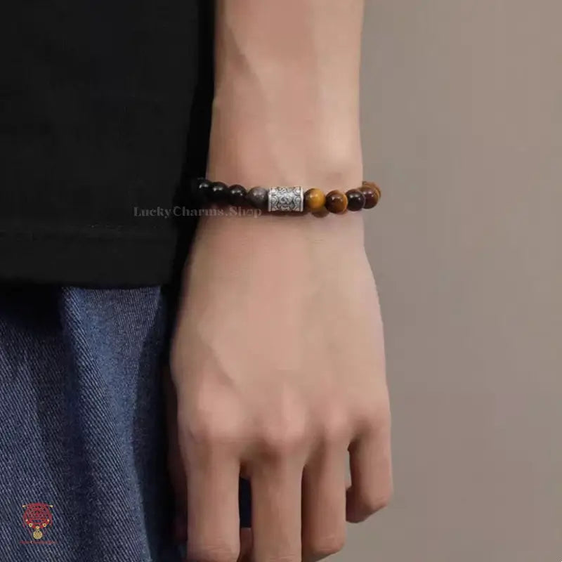 Close-up of a man wearing a yellow and blue tiger's eye beaded healing bracelet with a silver cylinder charm.