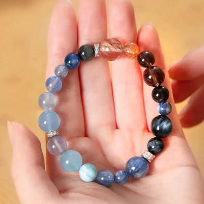 Water element crystal bracelet in hand with aquamarine, kyanite, obsidian, and black super seven beads.