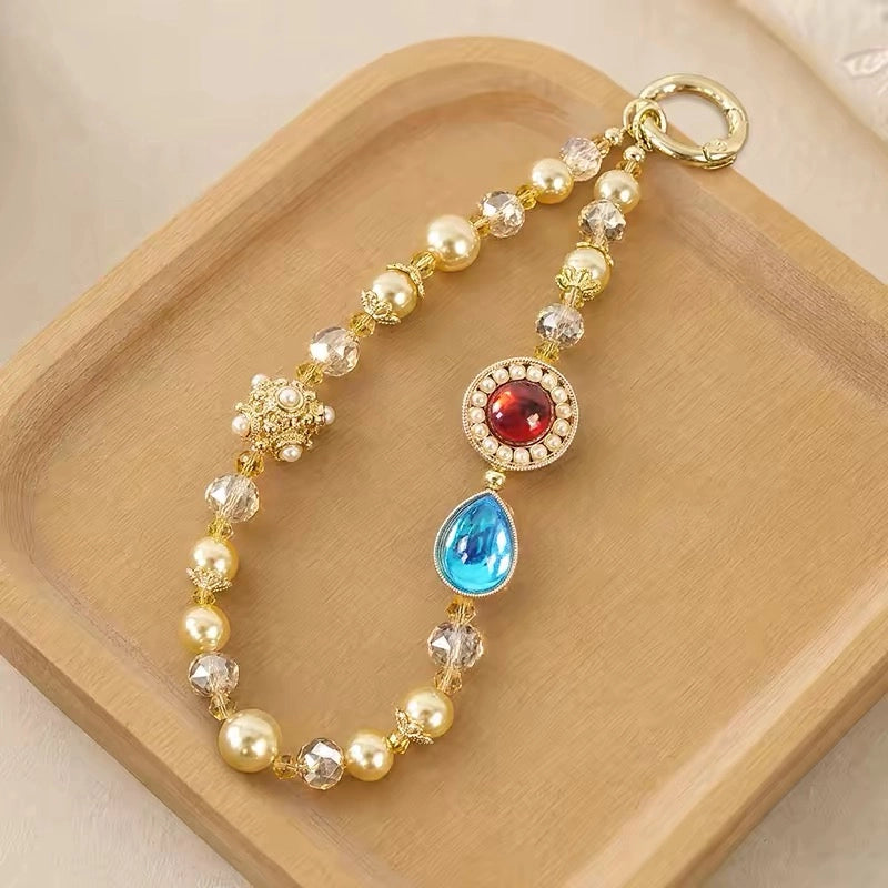 Chinese style beaded phone lanyard with red gem and blue teardrop charm on wooden display.