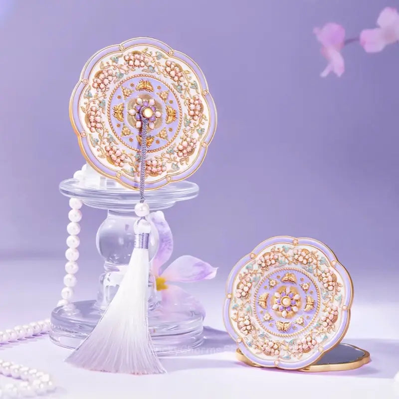 Palace Museum purple floral butterfly portable folding compact mirror with tassel accent on glass stand.