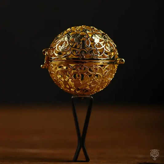 Gold Chinese hollowed incense sphere car air vent clip diffuser on a dark background.