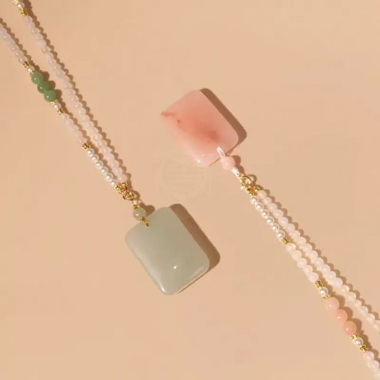 Flat lay view of green jade and pink crystal rectangular pendant necklaces with pearl beads.