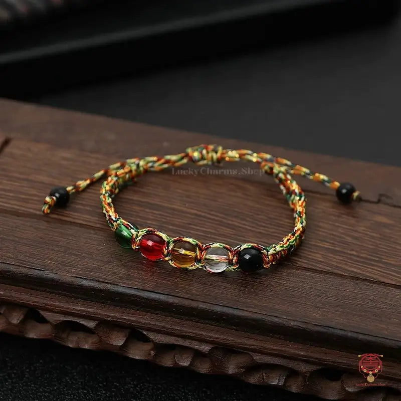Fully extended handmade mindfulness knot bracelet with green, red, yellow, and clear beads on a wood background.