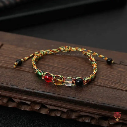 Fully extended handmade mindfulness knot bracelet with green, red, yellow, and clear beads on a wood background.