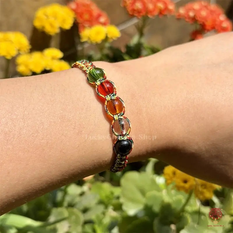 A person wearing the five elements protection rope bracelet on their wrist against a sunny flower background.